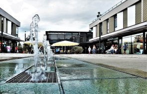 Neu Mitte Wasserfontänen in einem modernen, offenen Platz mit umliegenden Gebäuden und Menschen im Hintergrund