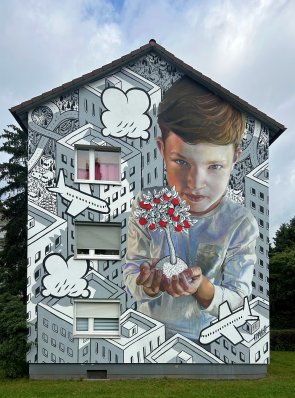 Urban Art Großflächiges Wandbild an einem Wohnhaus zeigt einen Jungen, der einen Baum mit roten Blättern in den Händen hält, umgeben von schwarz-weißen stilisierten Gebäuden, Wolken und Flugzeugen